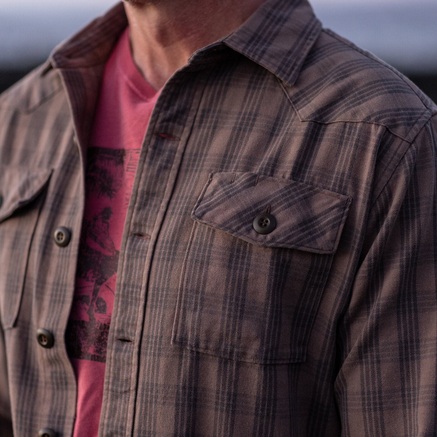 Person wearing a brown plaid shirt over a red garment with a blurred background