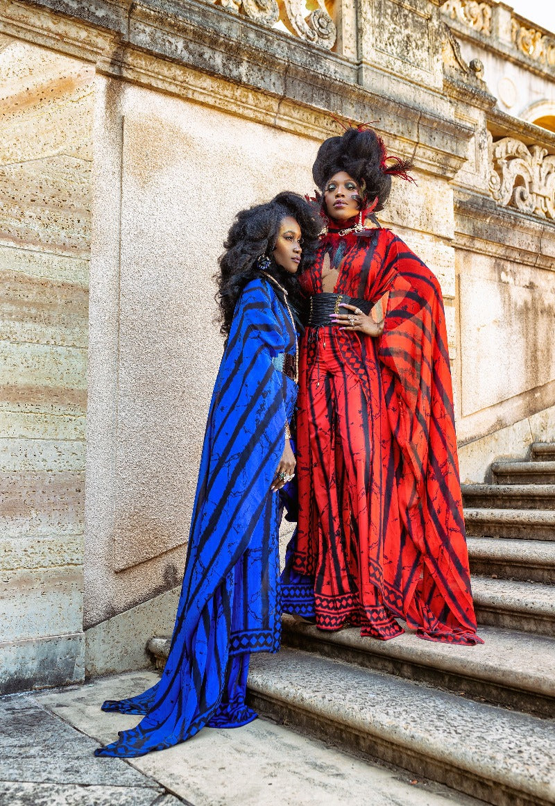 Two women in colorful striped dresses standing on stone steps with an ornate wall in the background.
