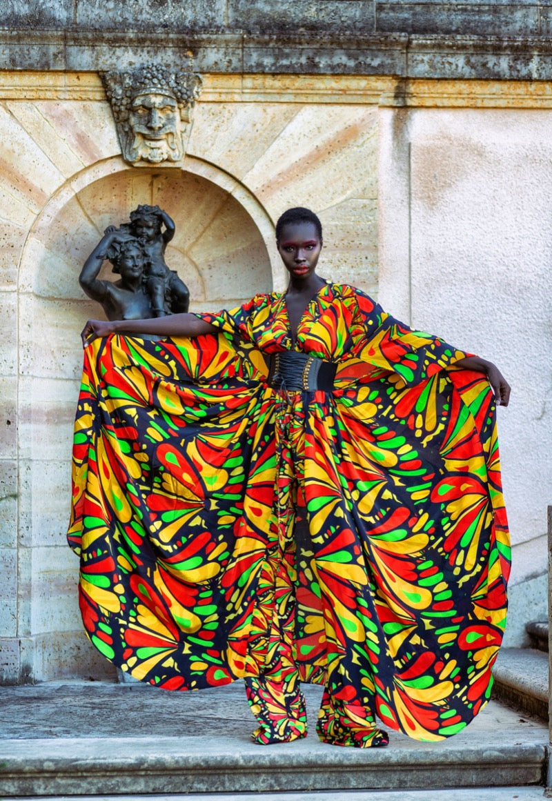 Person wearing a colorful patterned outfit standing in front of classical architecture.