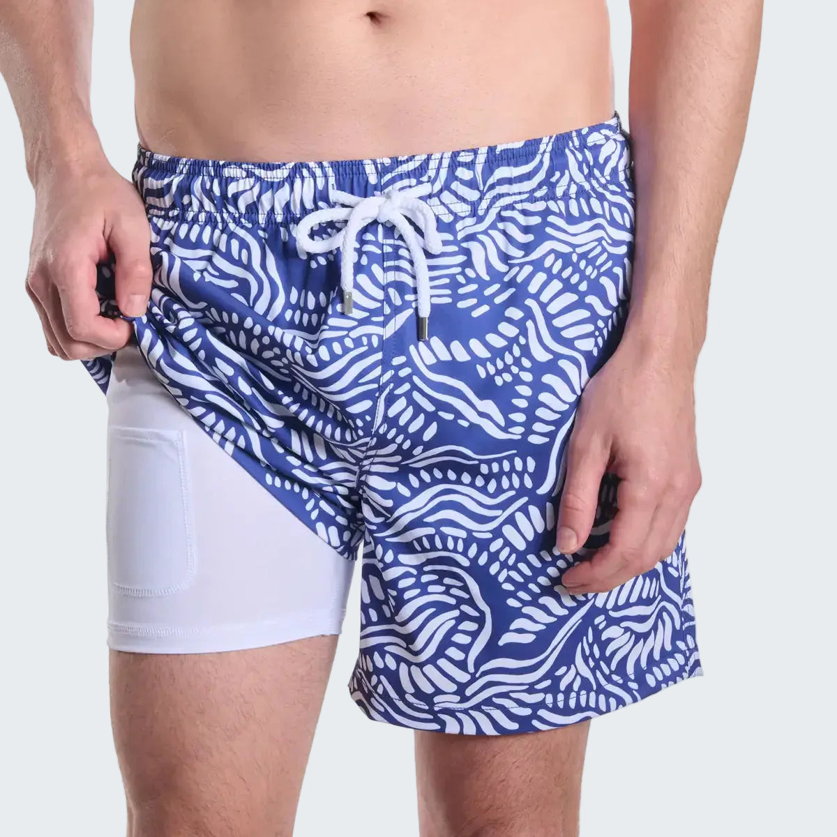 Blue and white patterned swim shorts worn by a person on a white background