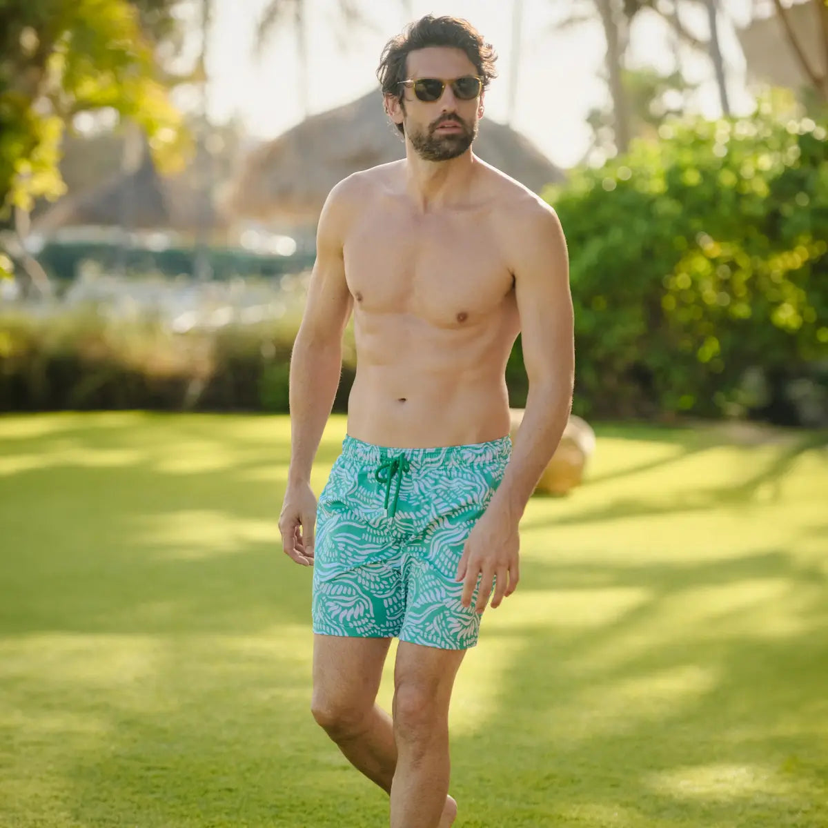 Man wearing teal swim shorts with a pattern walking on grass