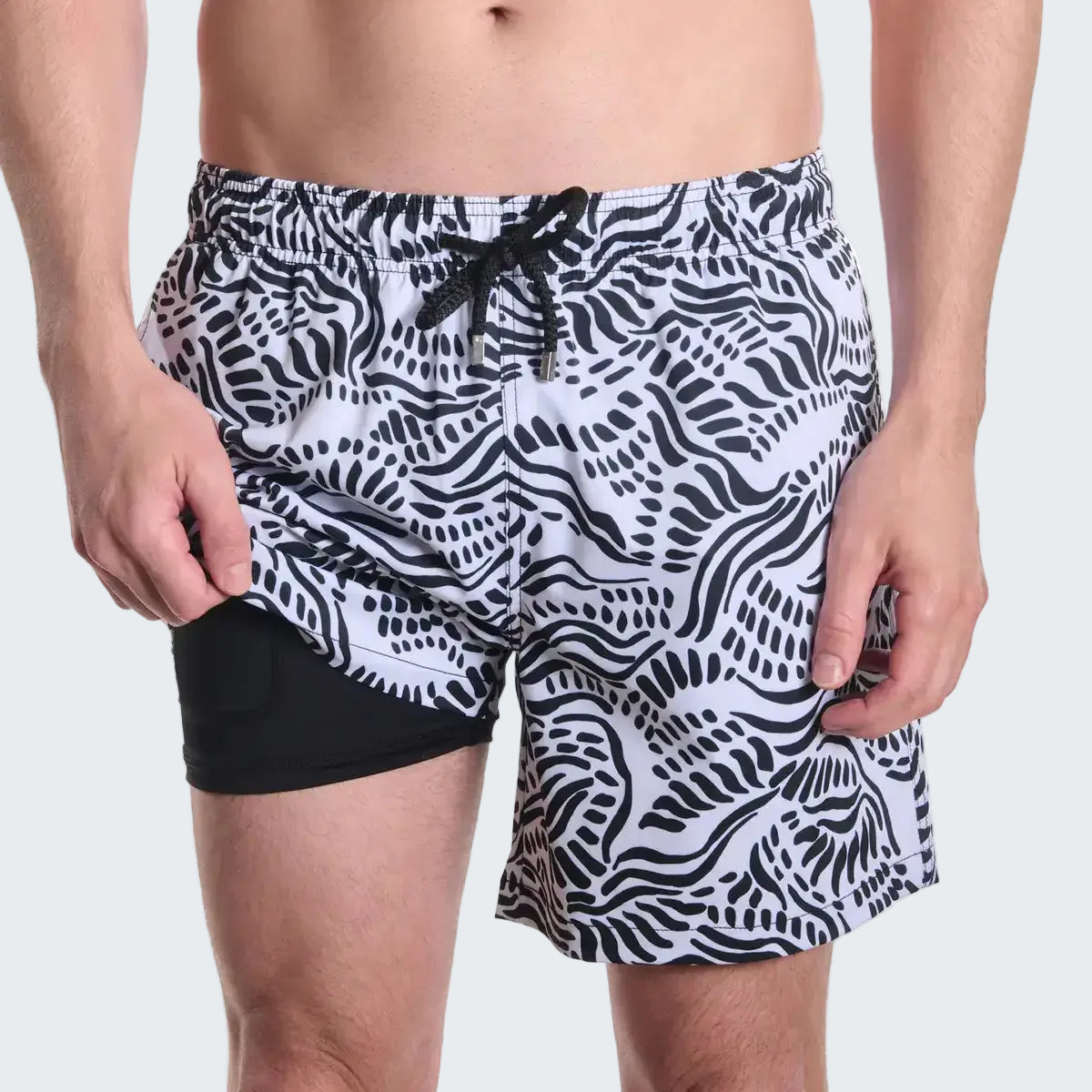 Black and white patterned swim shorts on a person against a white background