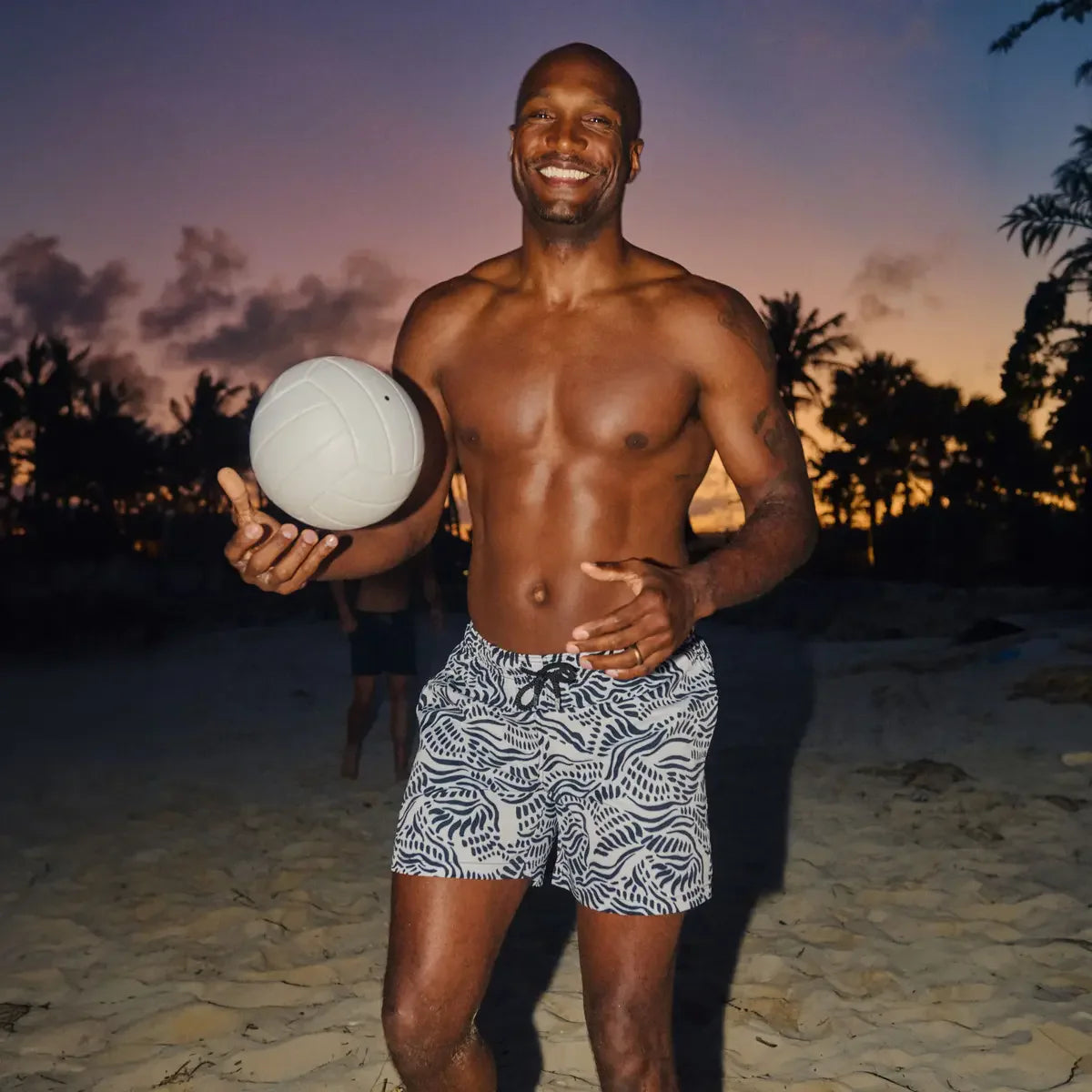 Man holding a volleyball on a beach at sunset