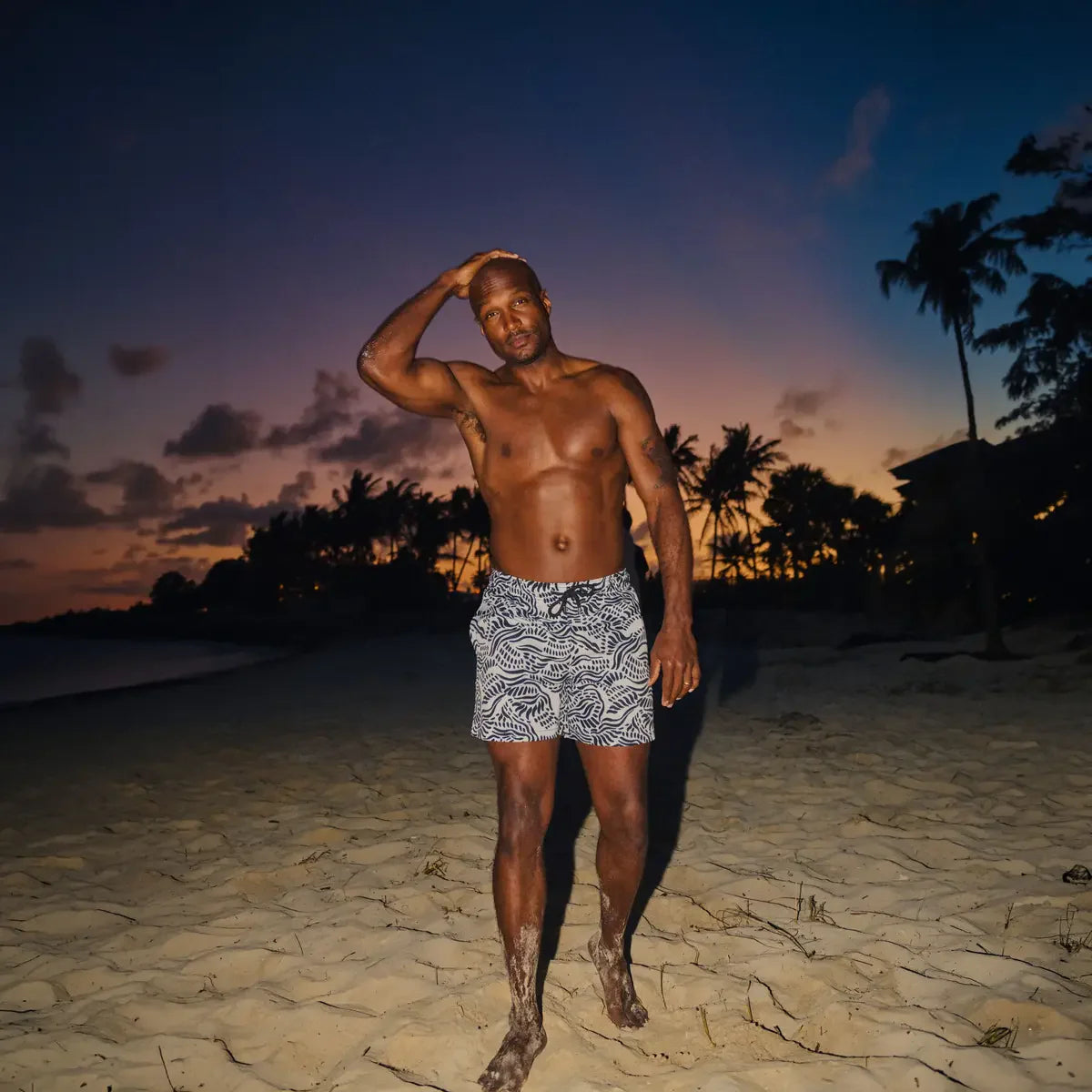 Man standing on a beach at sunset with palm trees in the background