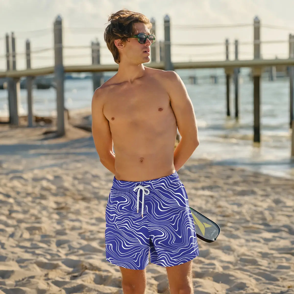 Man wearing blue swim shorts with wavy pattern on a sandy beach.