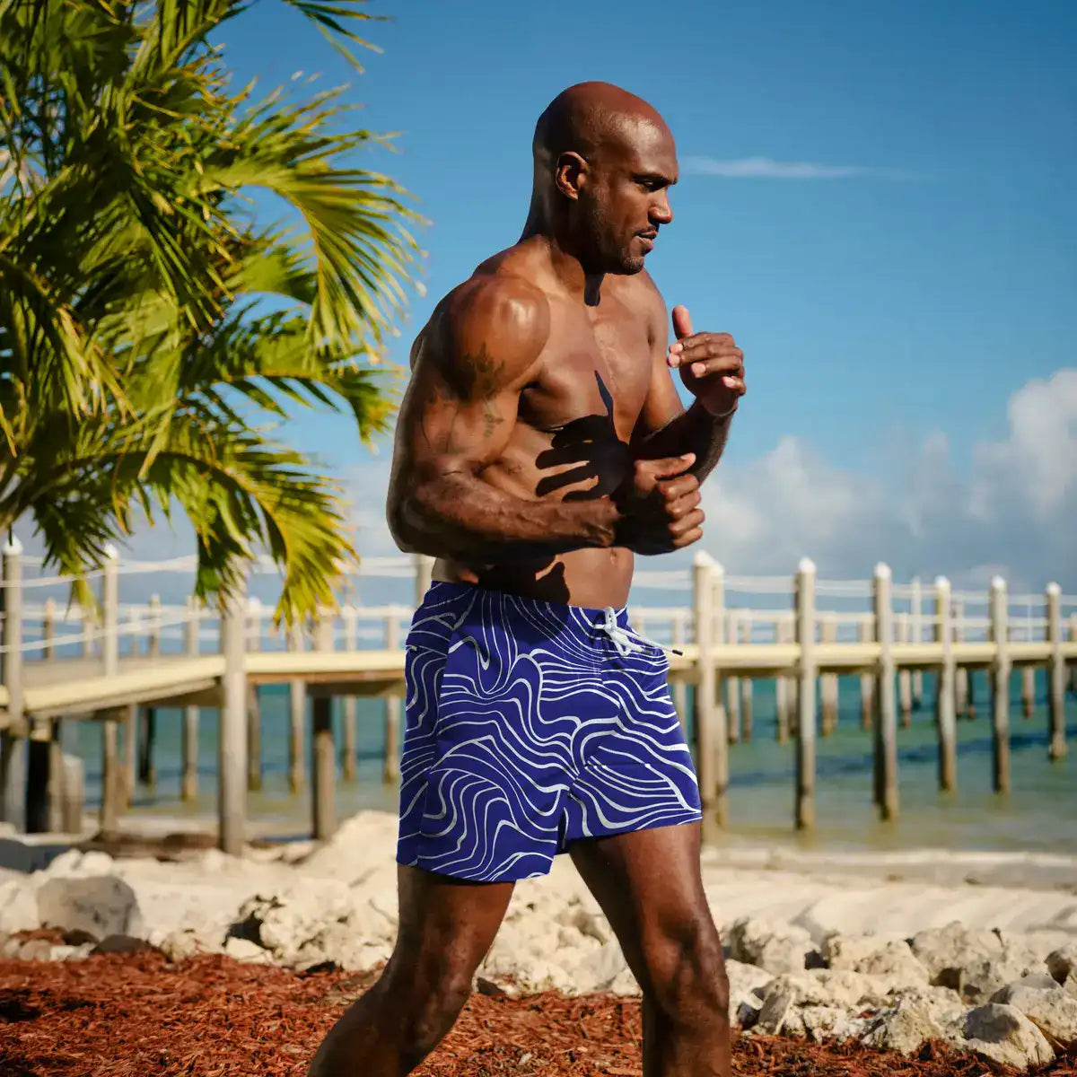 Man running on a beach with palm trees and a pier in the background