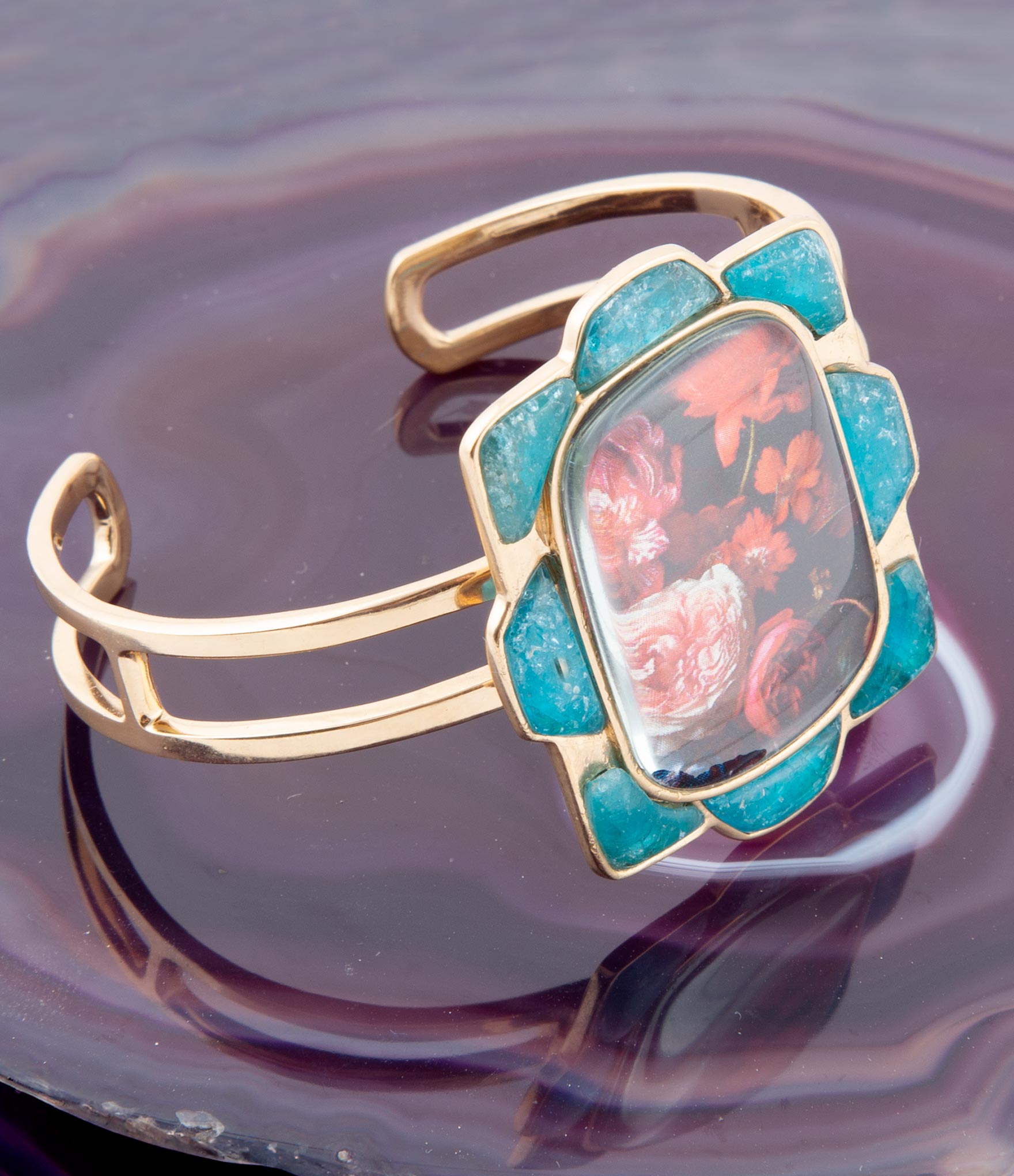 Gold bracelet with a blue stone featuring floral design on a reflective surface