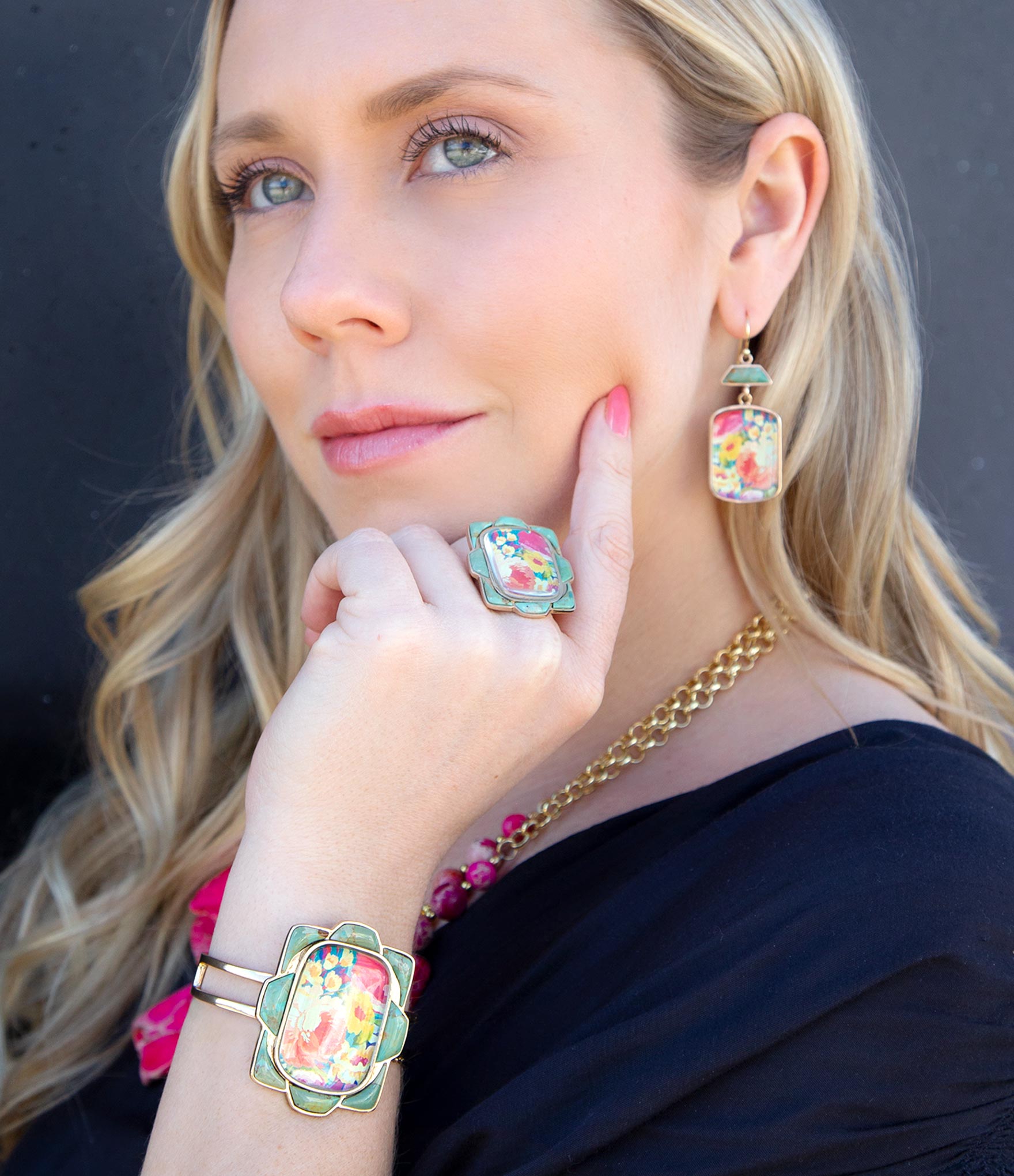 Woman wearing colorful floral earrings and a bracelet against a dark background