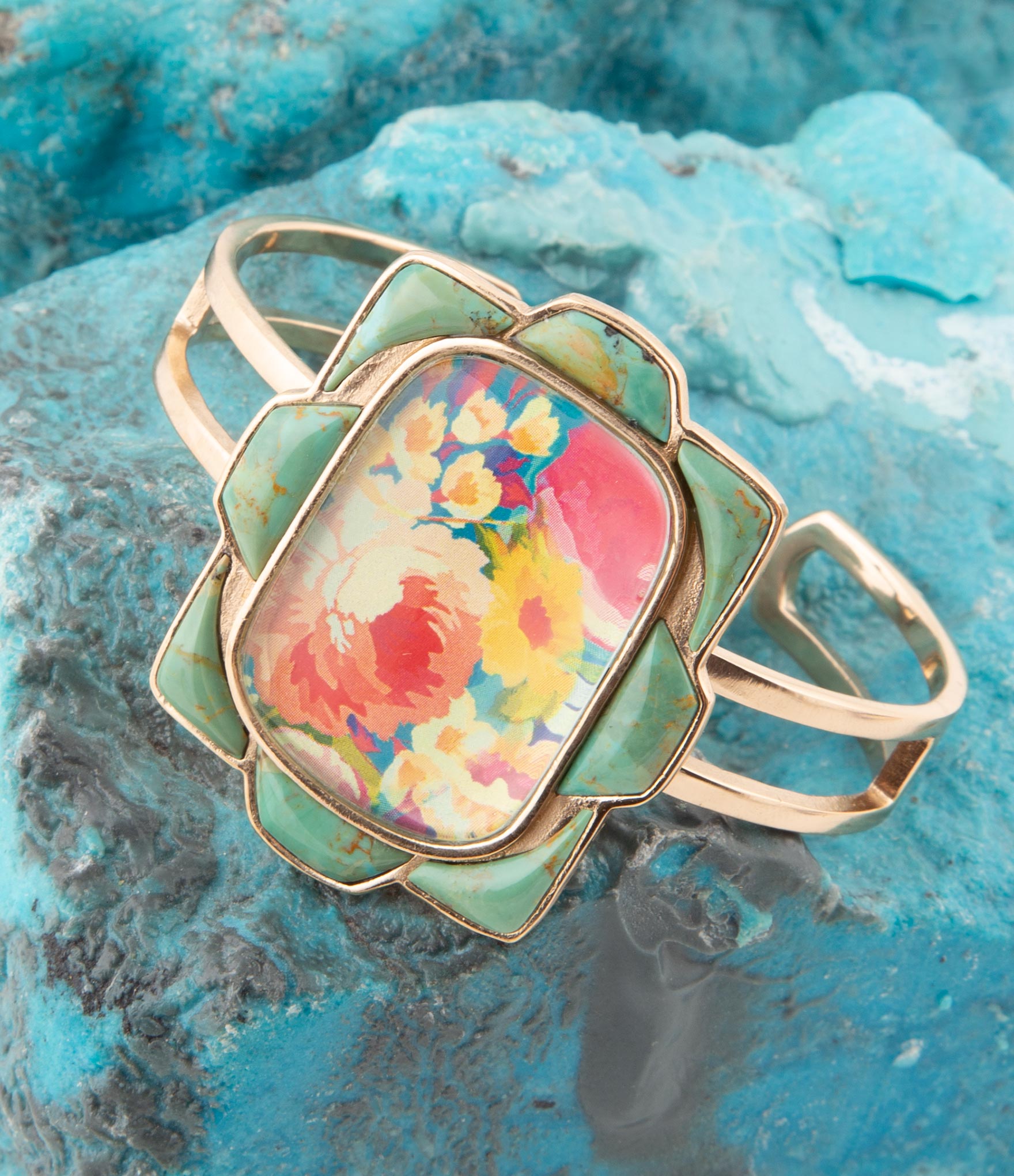 Gold ring with a colorful floral design on a textured blue surface
