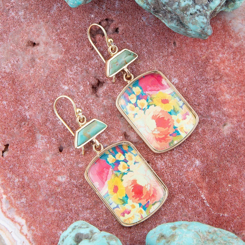 Floral earrings with gold accents on a pink stone background