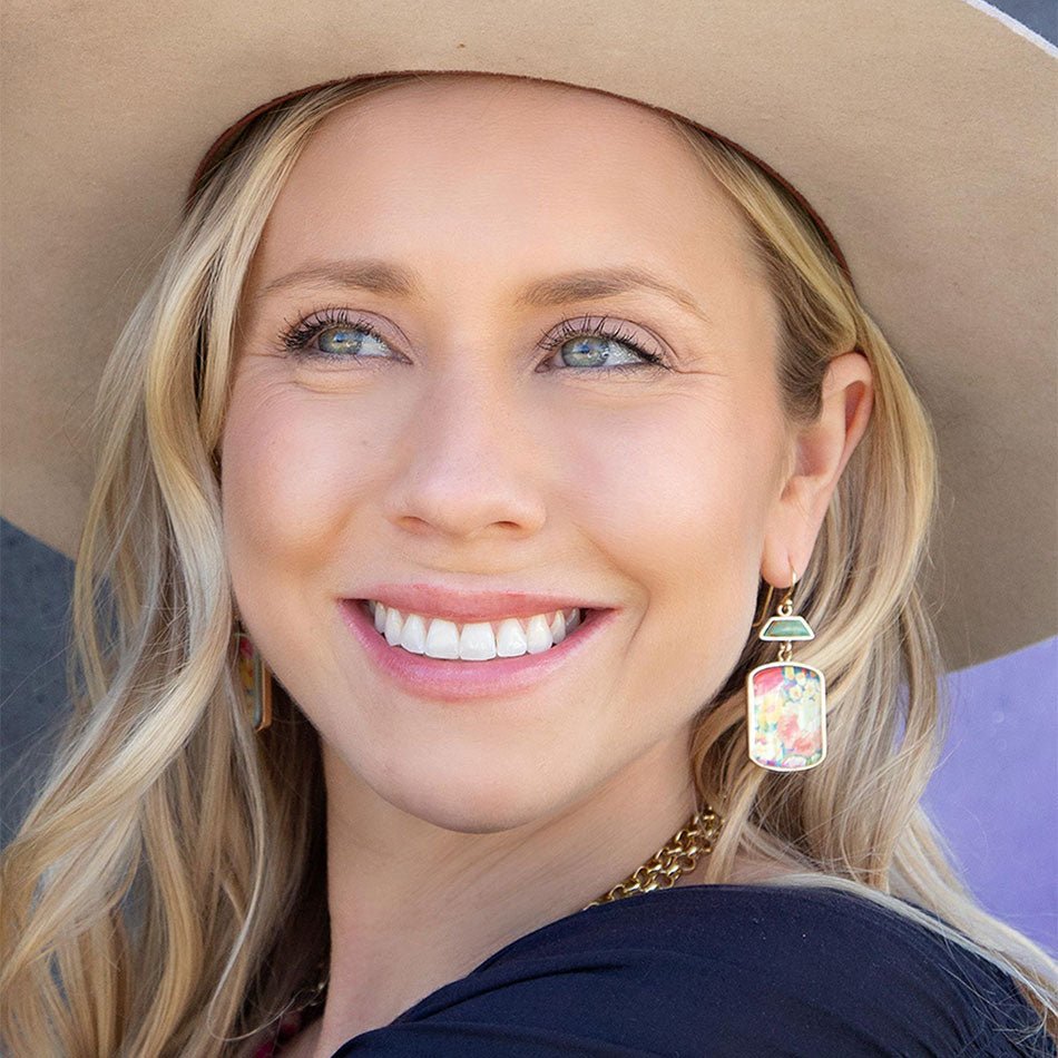 Woman wearing a wide-brimmed hat and colorful earrings, smiling.
