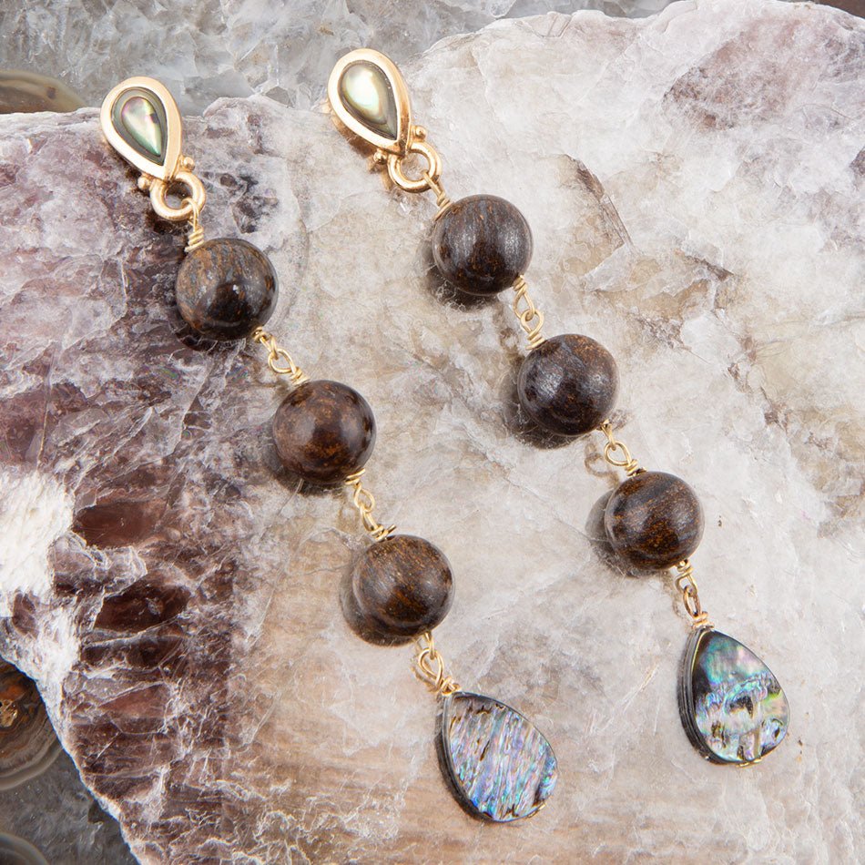 Gold earrings with brown beads and colorful teardrop-shaped stones on a stone surface