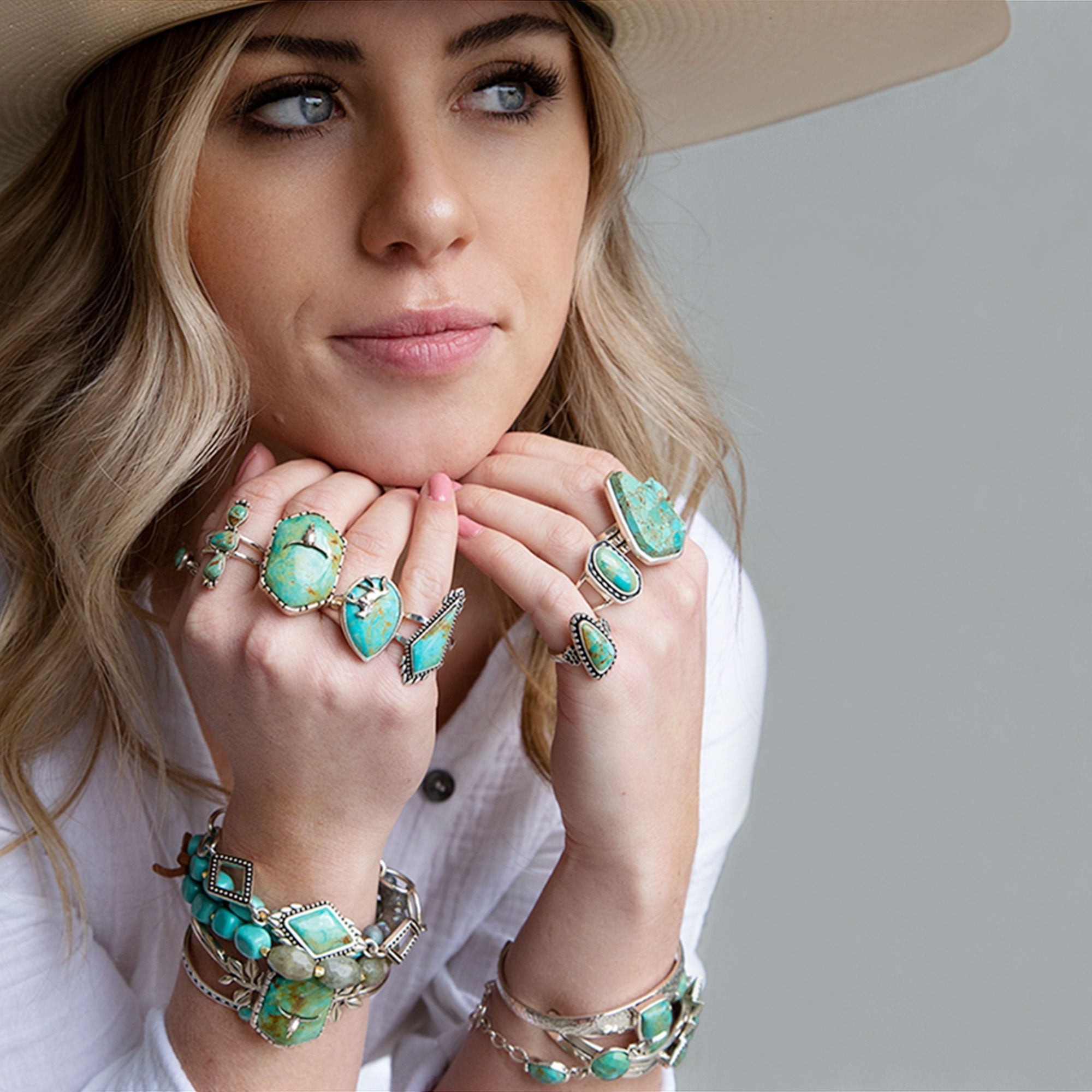 Woman wearing multiple turquoise jewelry pieces on a plain background