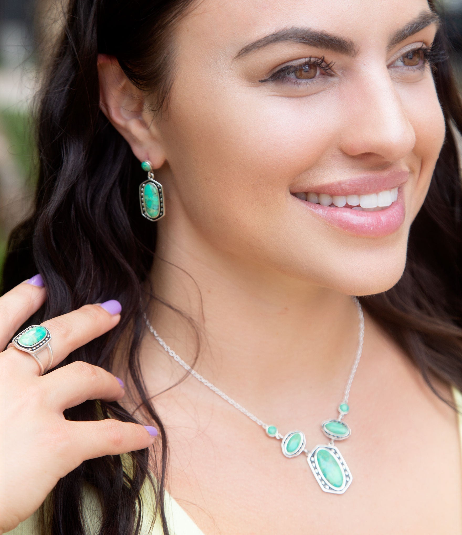 Woman wearing a silver necklace with green gemstones and matching earrings.