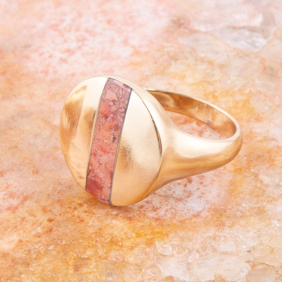 Gold ring with a pink stone on a textured beige surface