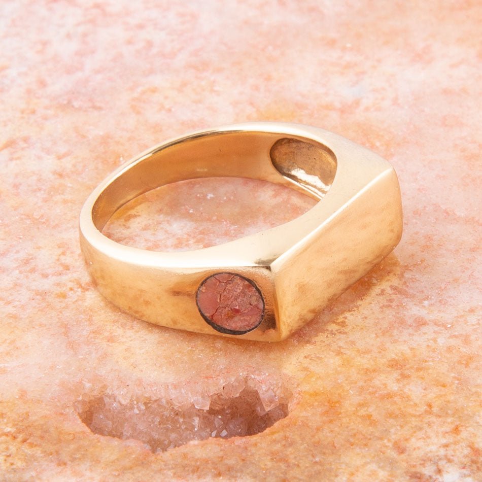 Gold ring with a red stone on a textured peach background