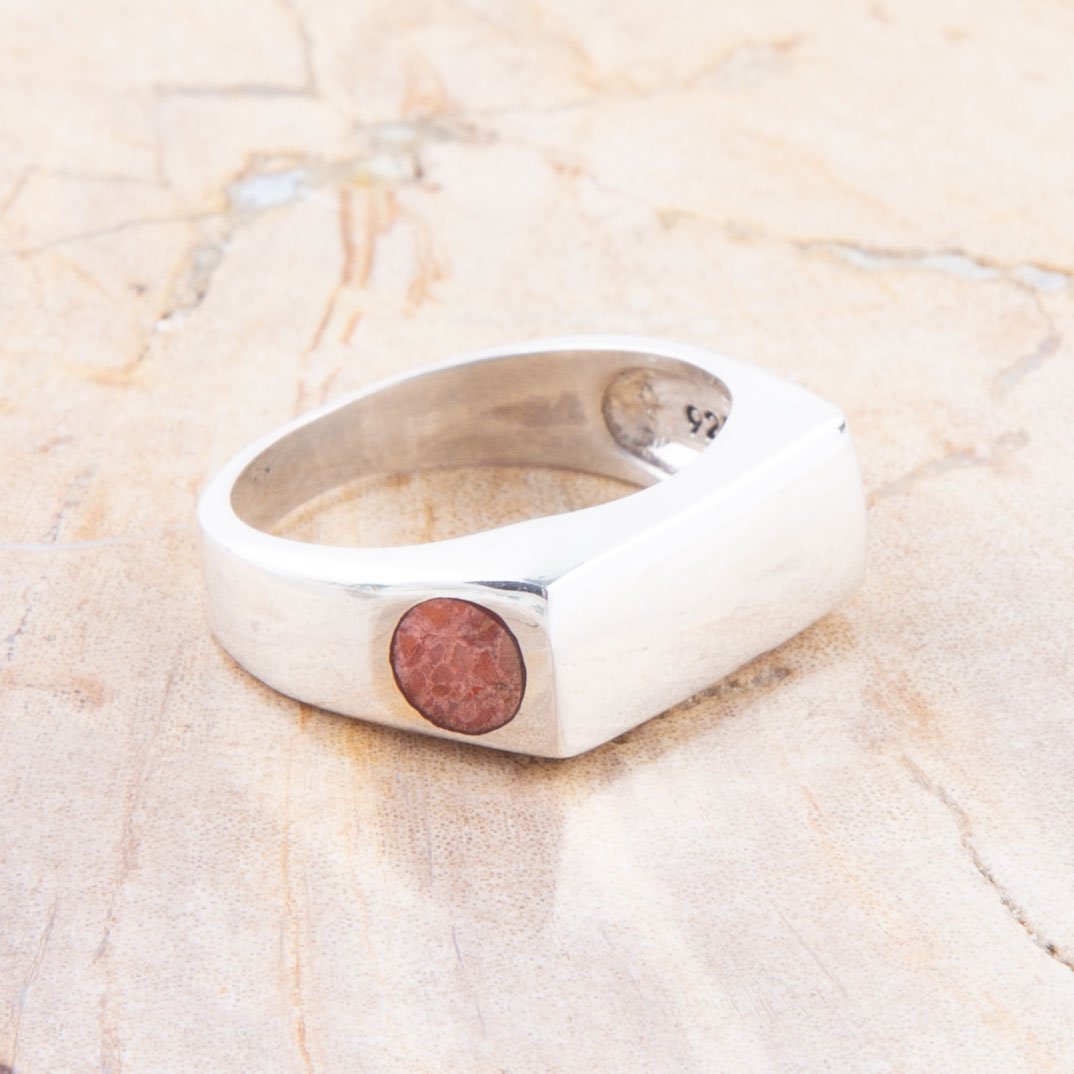 Silver ring with a circular pink stone on a beige stone surface