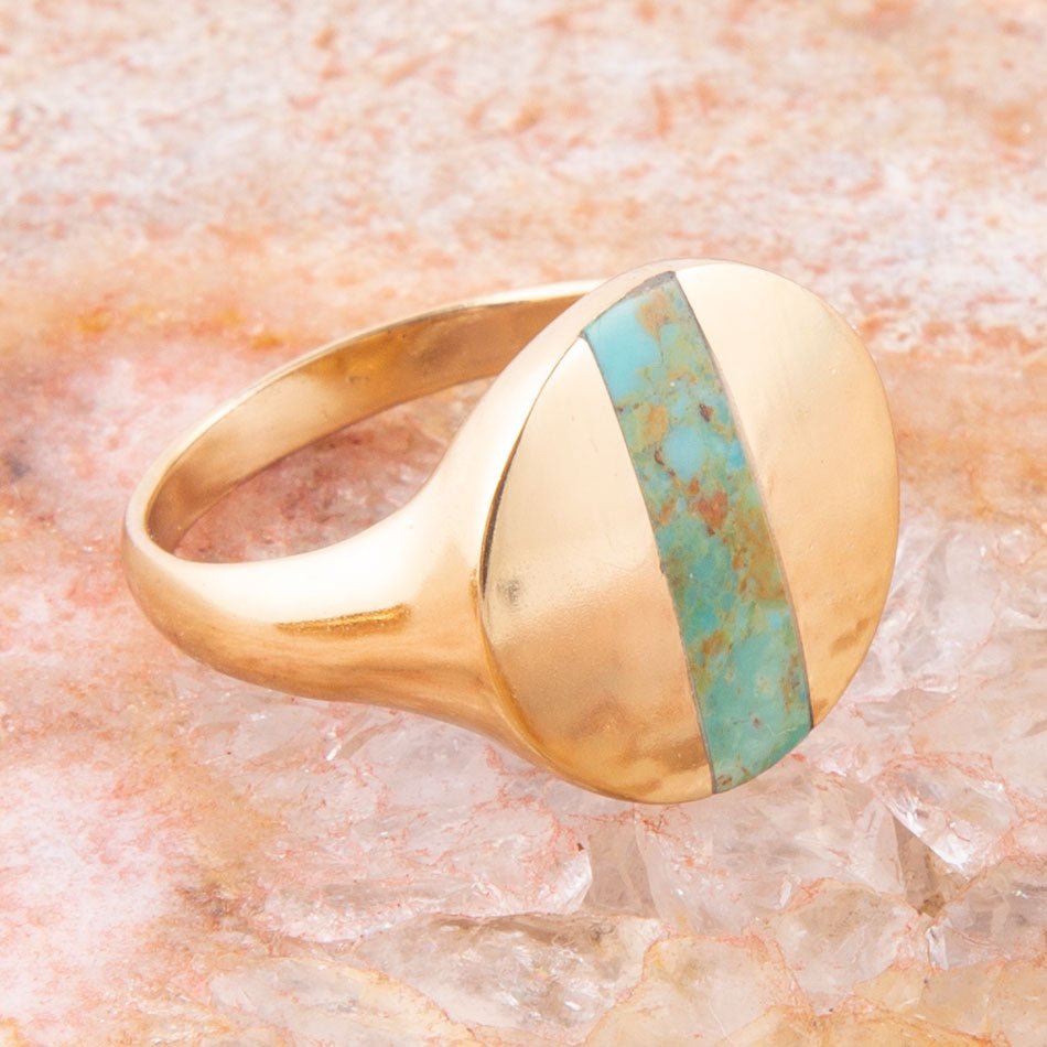 Gold ring with turquoise inlay on a textured stone surface