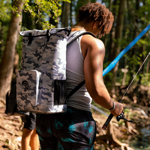 Person with a camouflage backpack walking outdoors near a body of water.