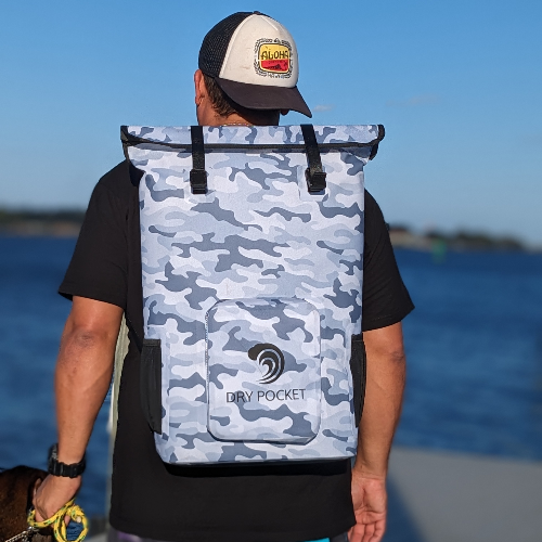 Person wearing a blue camouflage backpack with 'Dry Pocket' logo on a beach.