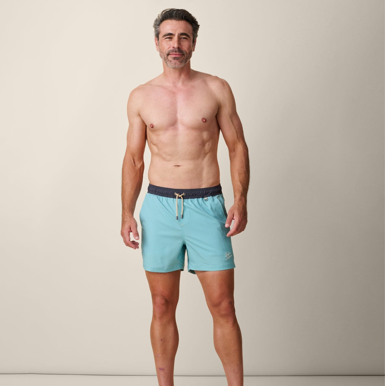 Man wearing light blue swim shorts with a dark belt against a neutral background