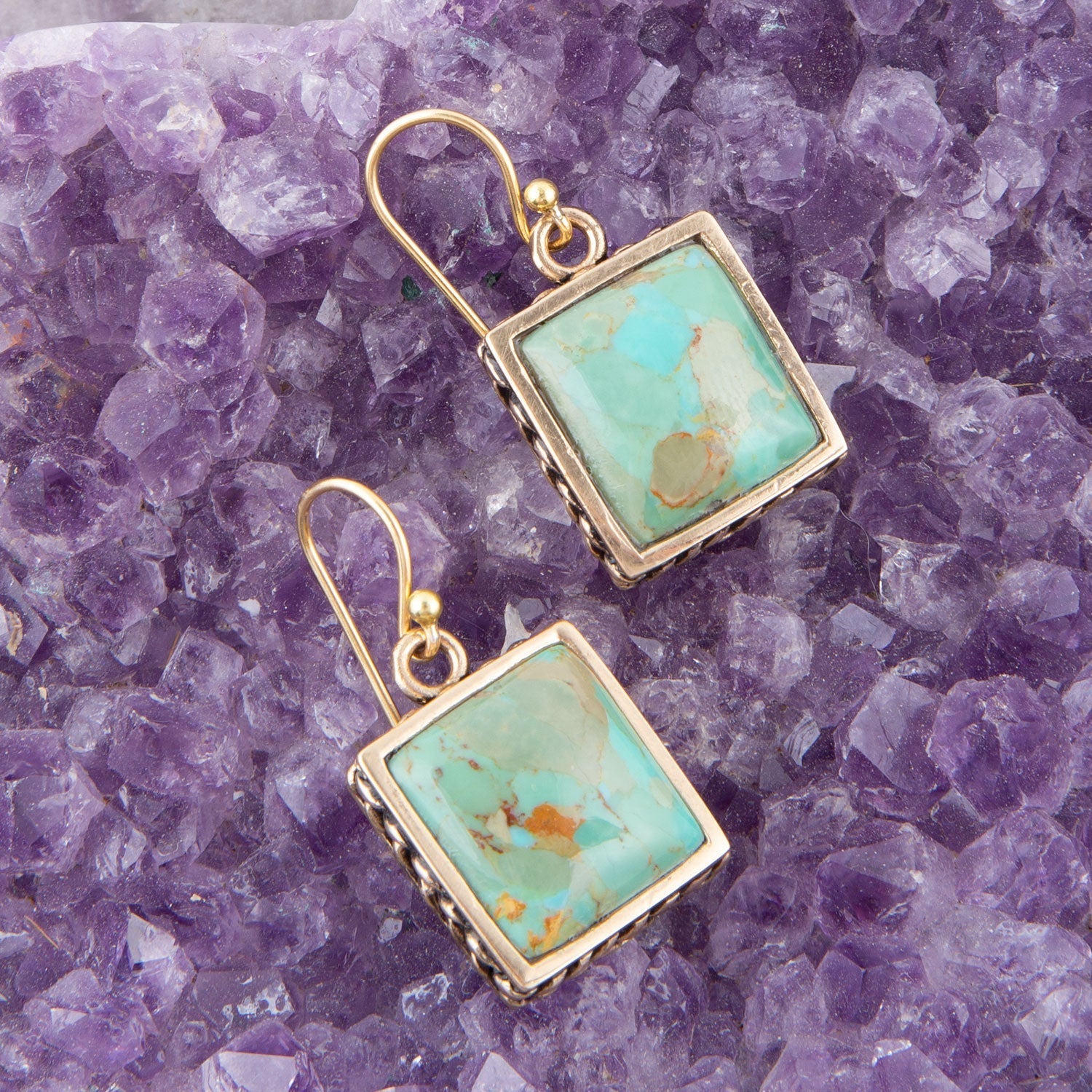 Gold-framed turquoise earrings on a purple crystal background