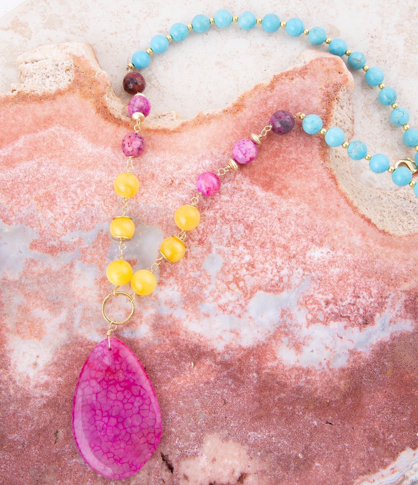 Necklace with colorful beads and a pink pendant on a textured surface