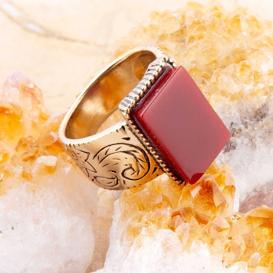 Gold ring with a red stone on a textured beige background