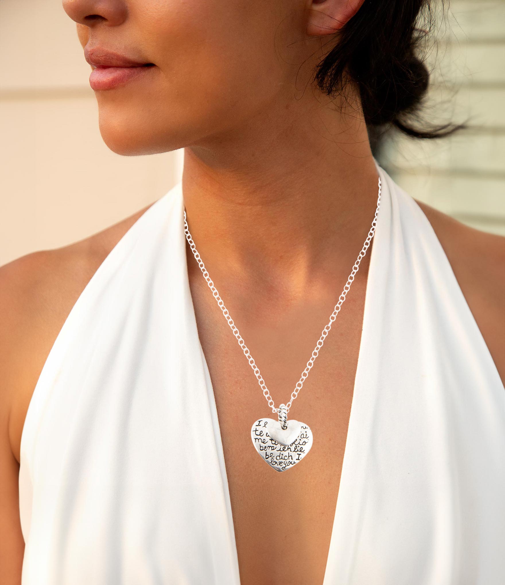 Silver heart-shaped pendant necklace worn by a person in a white top.