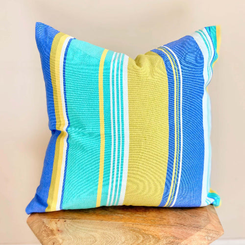 Striped pillow with blue, yellow, and green colors on a wooden surface.
