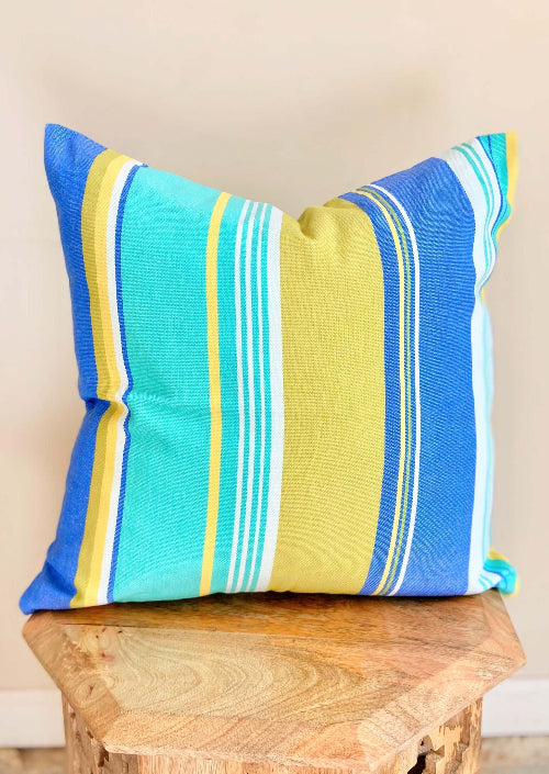 Colorful striped pillow on a wooden stool against a beige wall