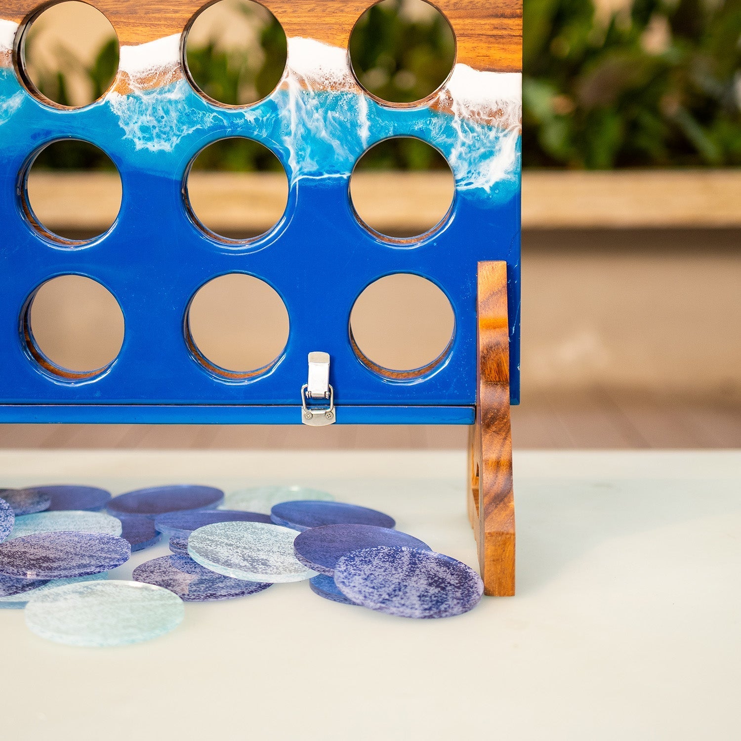 A blue and wood Connect-Five style game board with ocean-wave artwork, shown on a tabletop with round blue and purple game discs scattered in front.