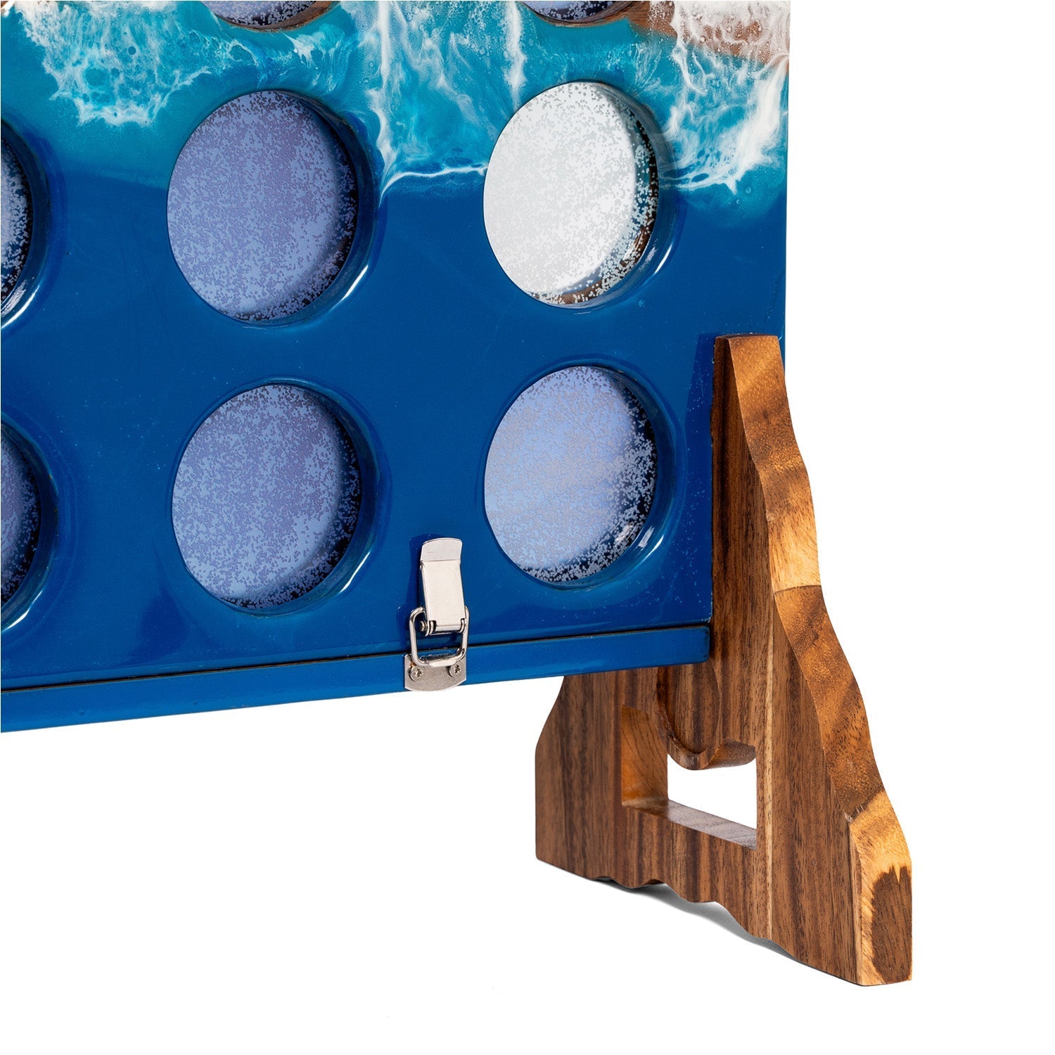 A close-up of a blue game board with circular holes, printed with ocean waves, supported by a wooden stand on a white background.