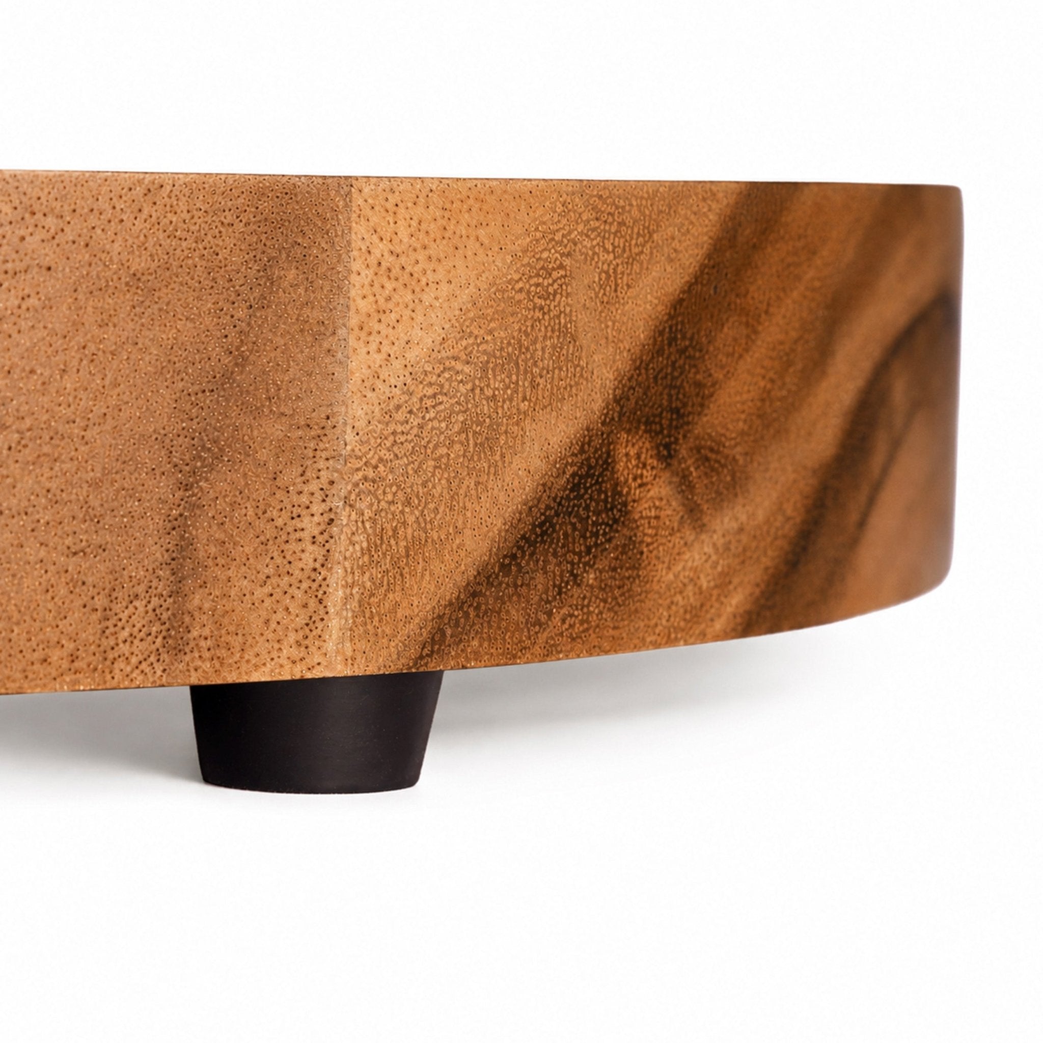 A close-up of a modern curved wooden furniture piece, likely a coffee table or bench, featuring a rich brown wood grain top and a matte black cylindrical base, set against a clean white background.