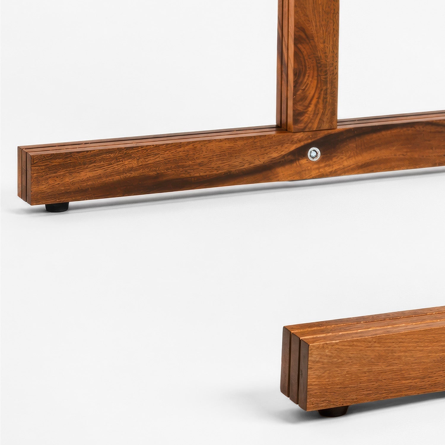 Close-up of a wooden furniture leg or frame component with a warm medium-brown wood grain finish, black feet, and a visible silver screw, photographed on a clean white studio background.