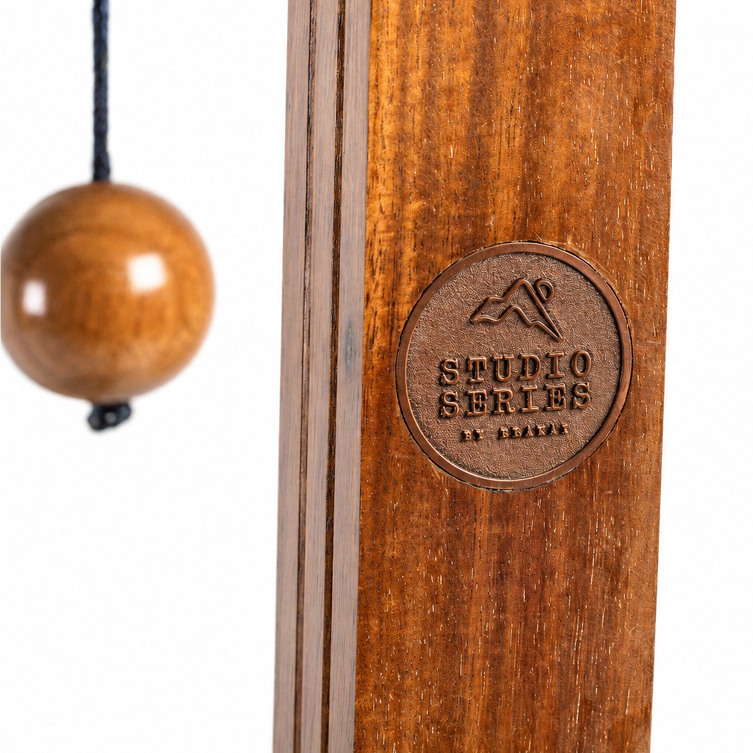 Close-up of a wooden studio percussion instrument, showing a round wooden mallet hanging on the left and a circular embossed logo reading 'STUDIO SERIES' on the wooden body, against a white background.