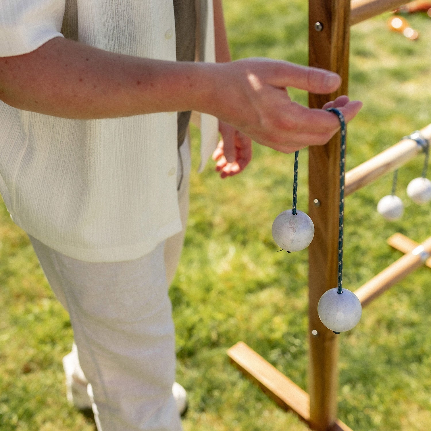 A person outdoors holding a wooden post with hanging white spherical objects on blue cords, with grass visible in the background.