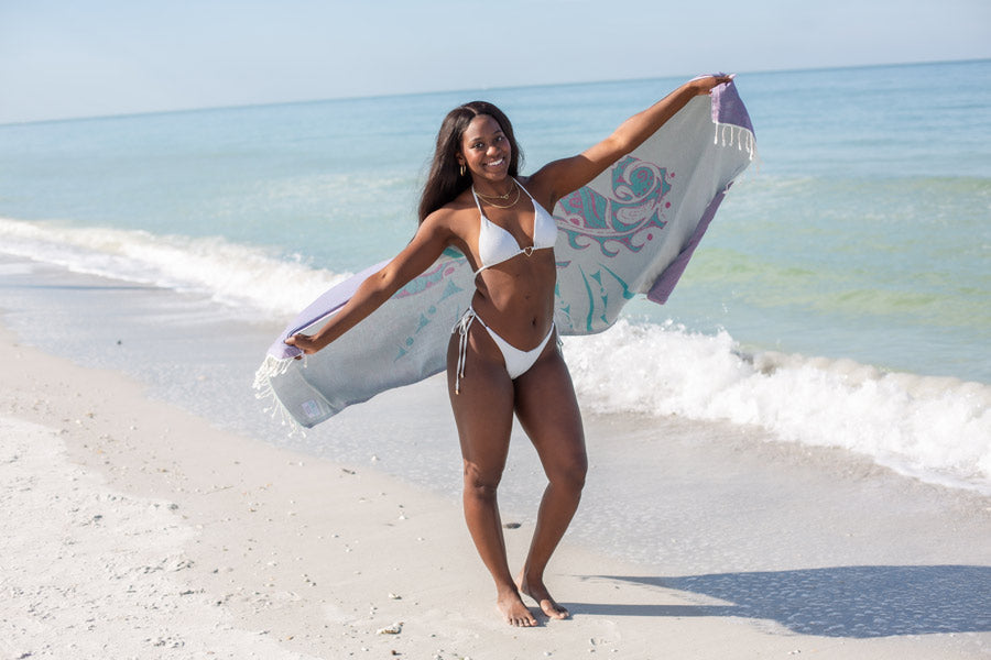 Woman in a white bikini holding a towel on a beach with ocean waves in the background