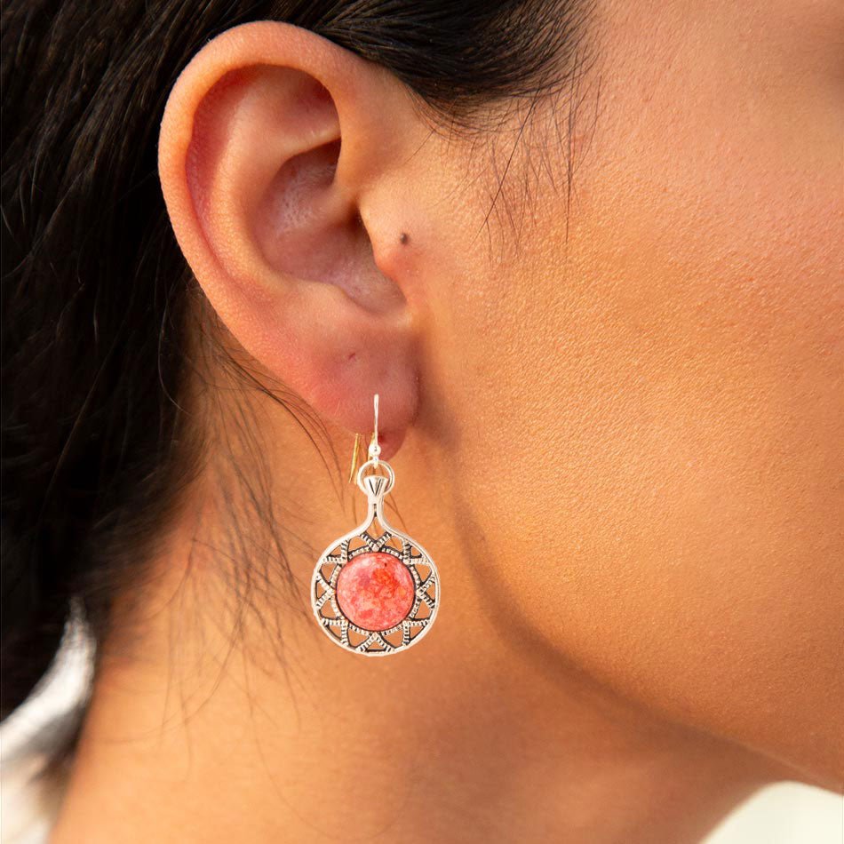 Close-up of an ear wearing a pink stone earring with silver detailing.