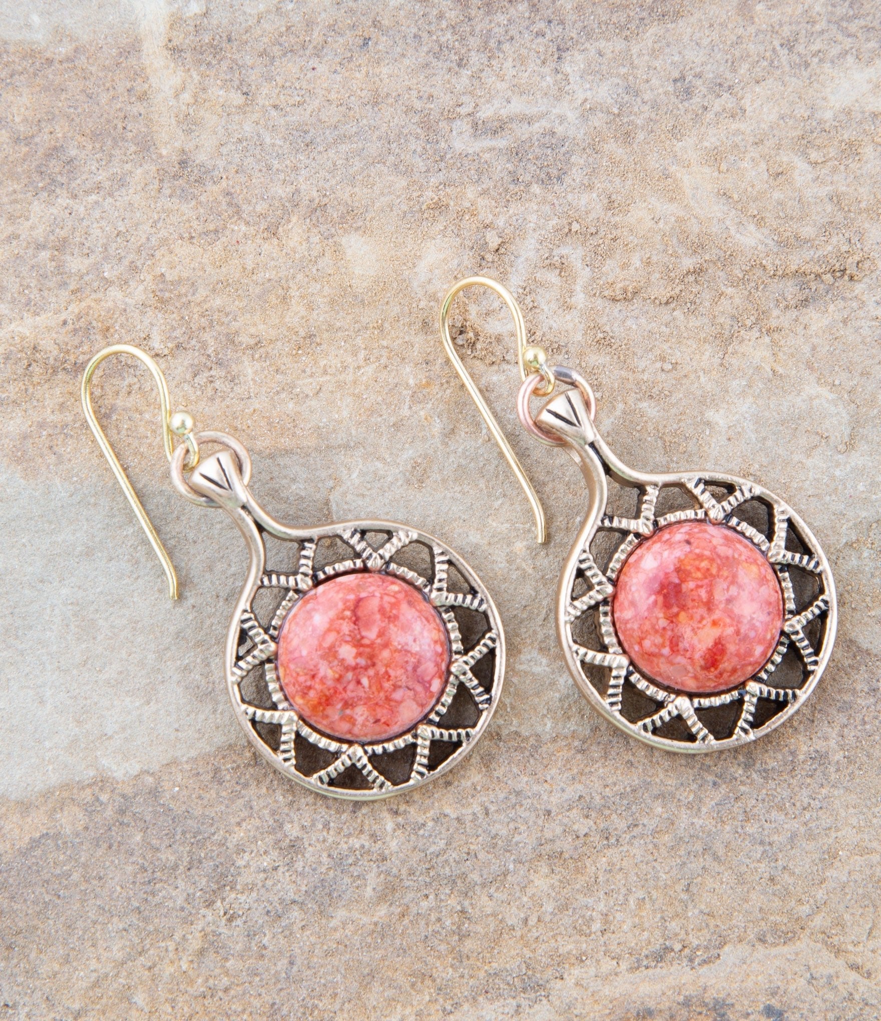 Pair of earrings with pink stone and decorative metalwork on a stone surface