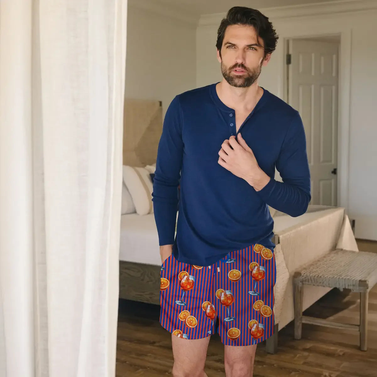 Man wearing a blue long-sleeve shirt and colorful shorts in a bedroom.