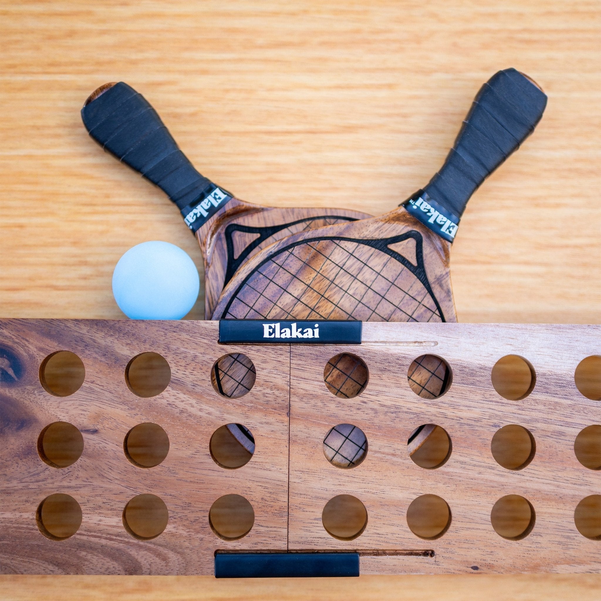 Wooden paddle and ball on a wooden surface with 'Elakai' branding.