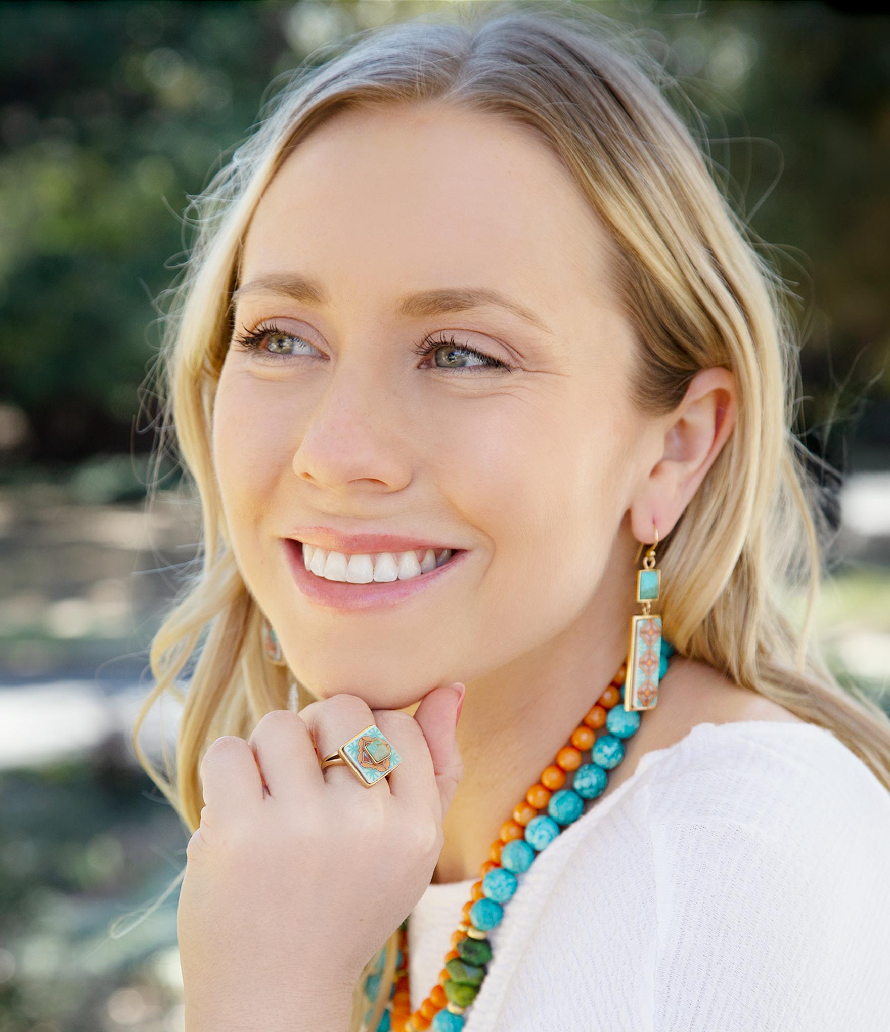 Woman wearing colorful jewelry including earrings, a necklace, and a ring outdoors.