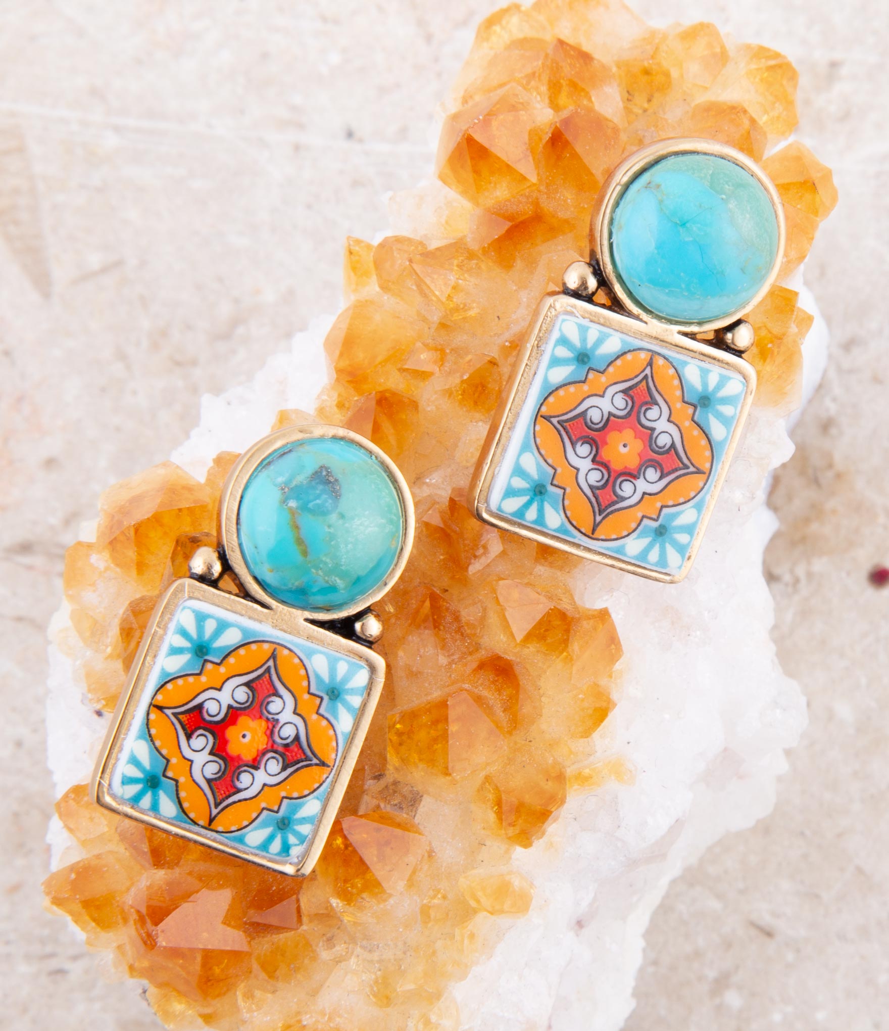 Colorful earrings with square designs and turquoise stones on a decorative stone background