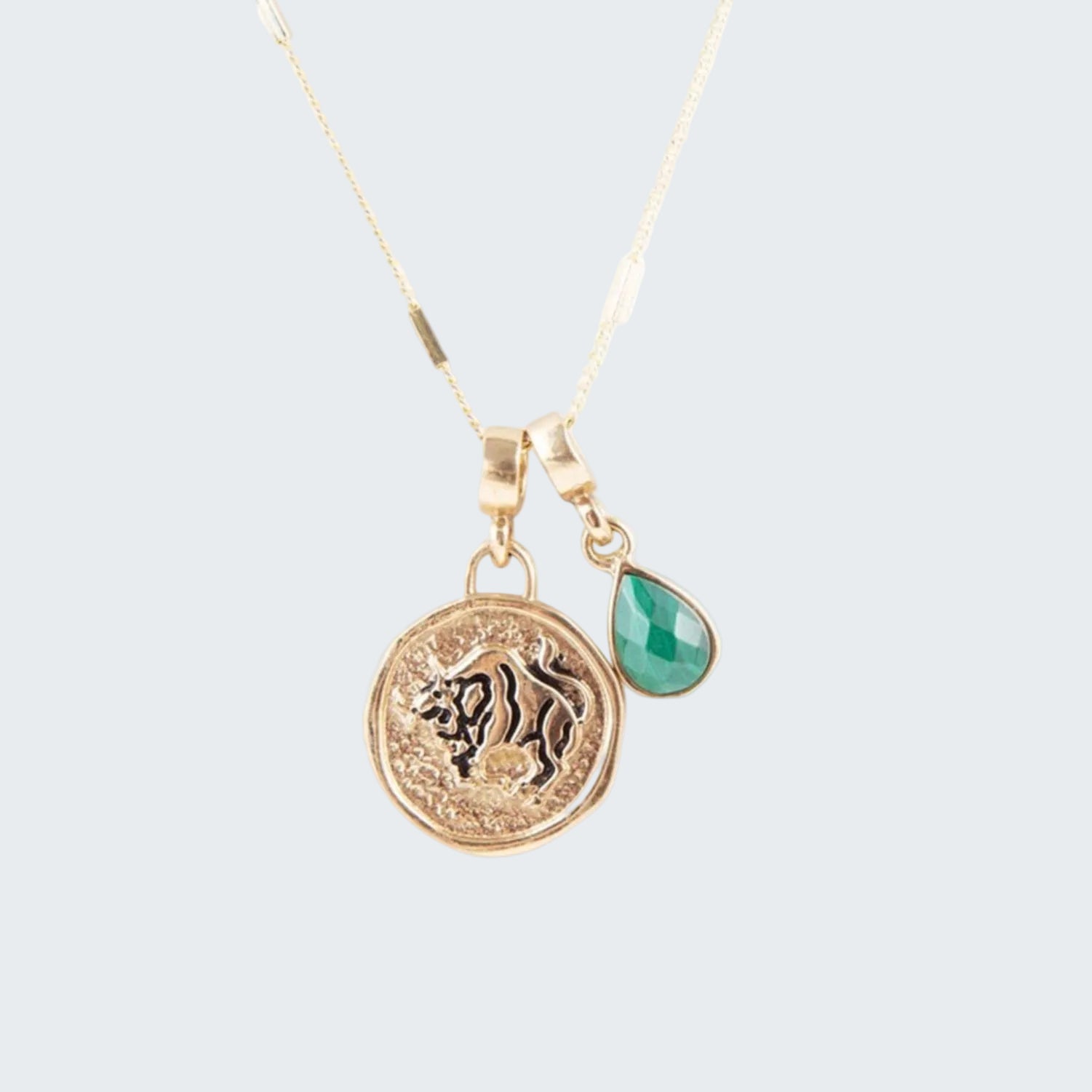 Gold necklace with lion emblem and green teardrop pendant on a white background