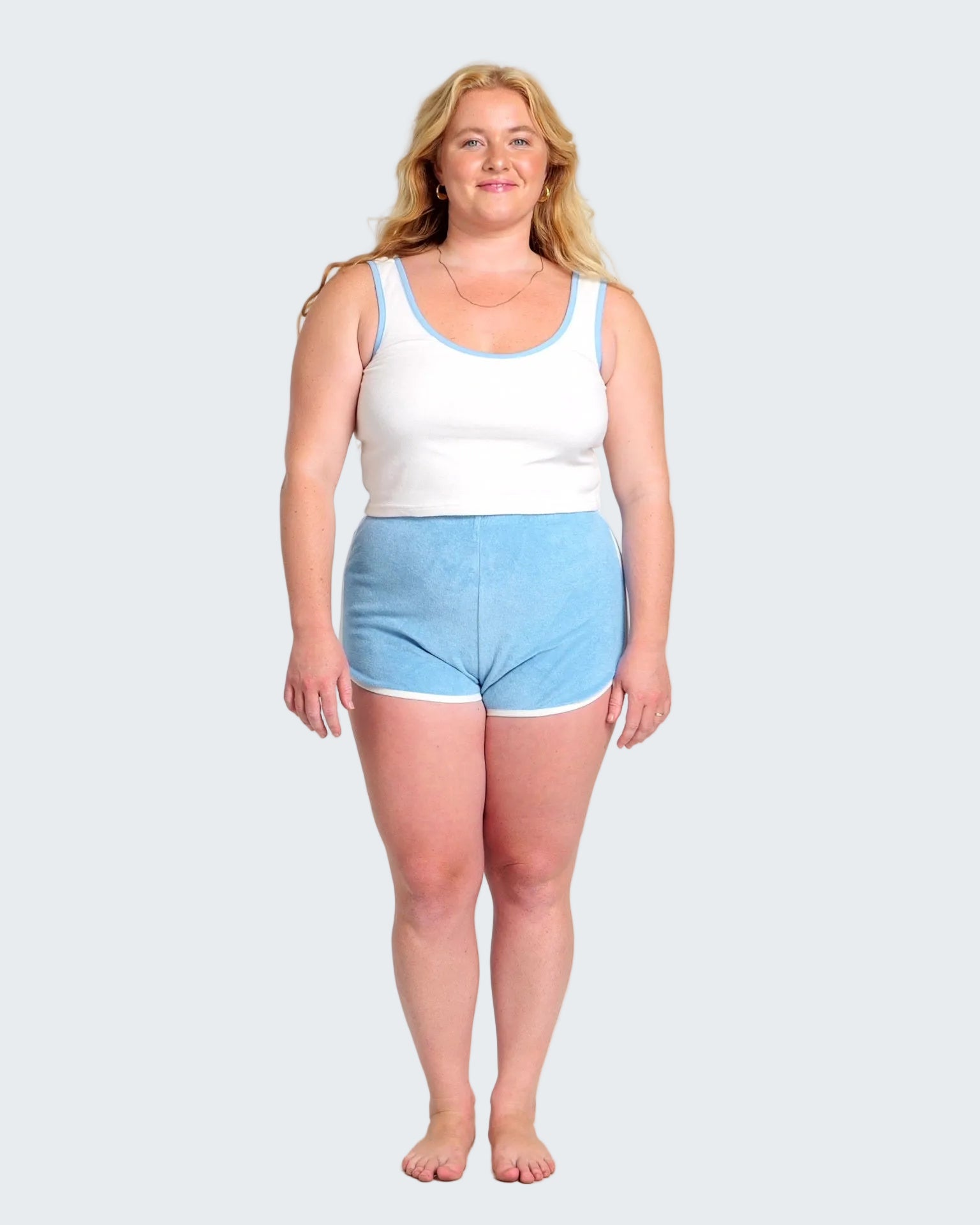Woman wearing a white tank top and light blue shorts on a white background