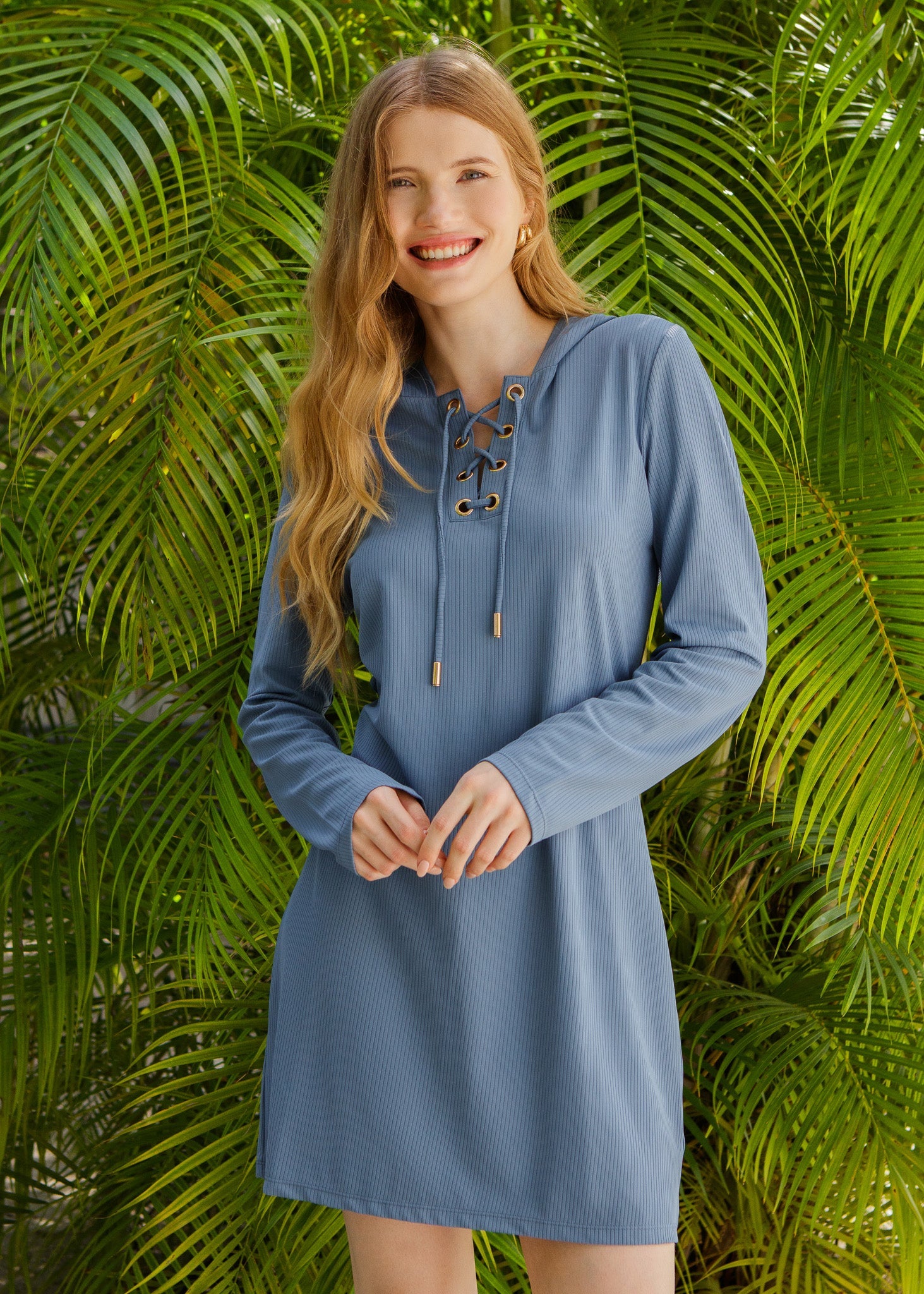 Woman wearing a blue dress with lace-up details against a green leafy background