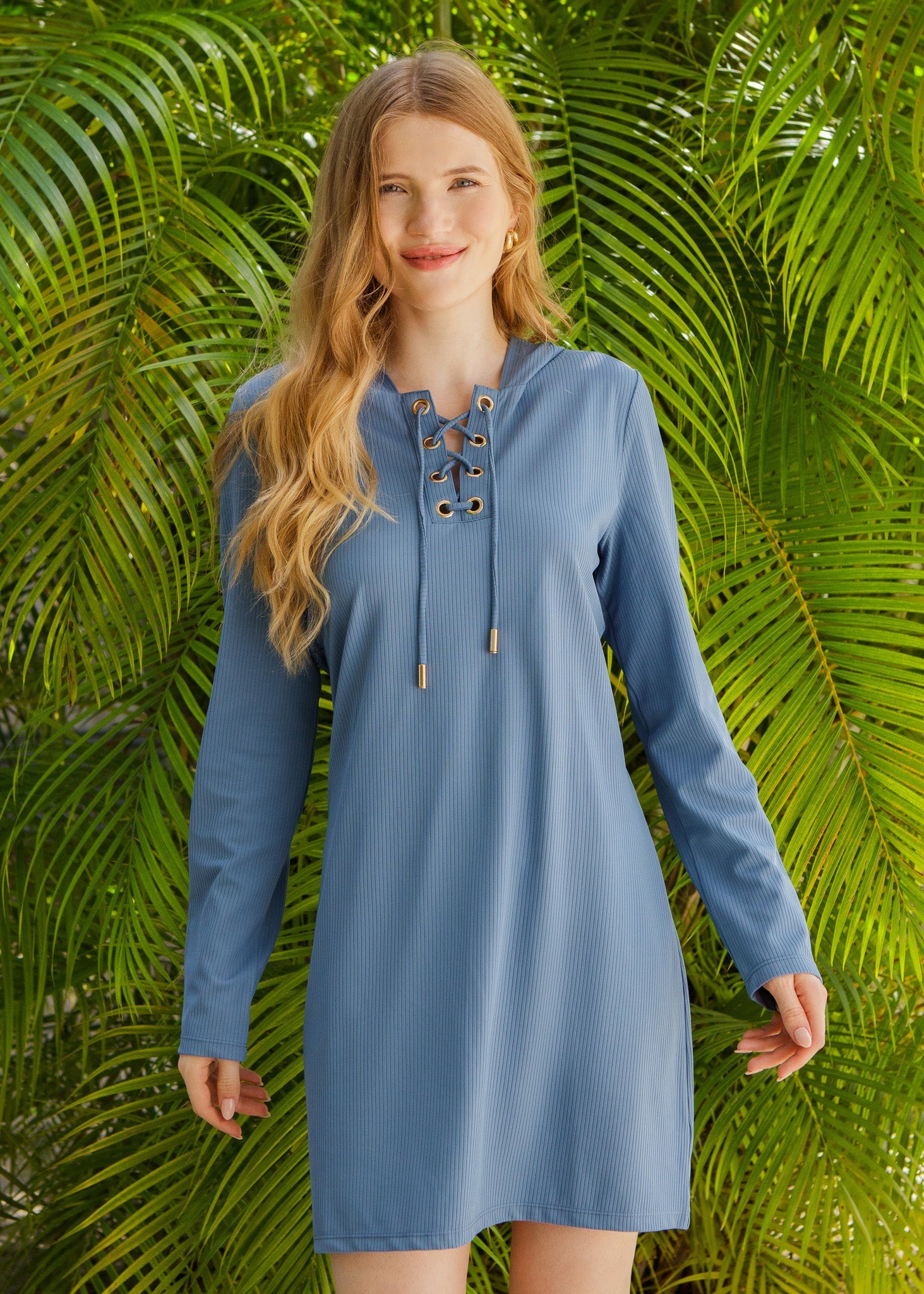 Woman wearing a blue dress with a lace-up front against a green leafy background