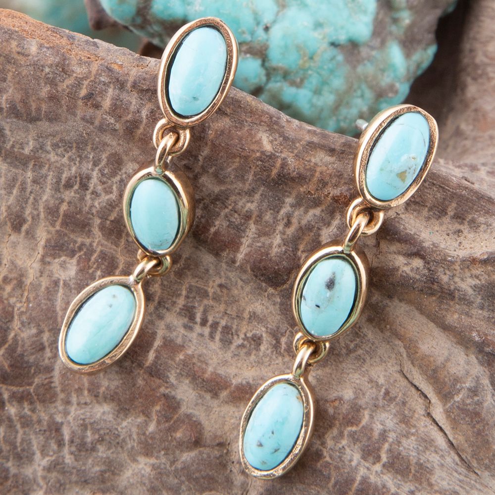 Turquoise earrings with gold accents on a stone surface