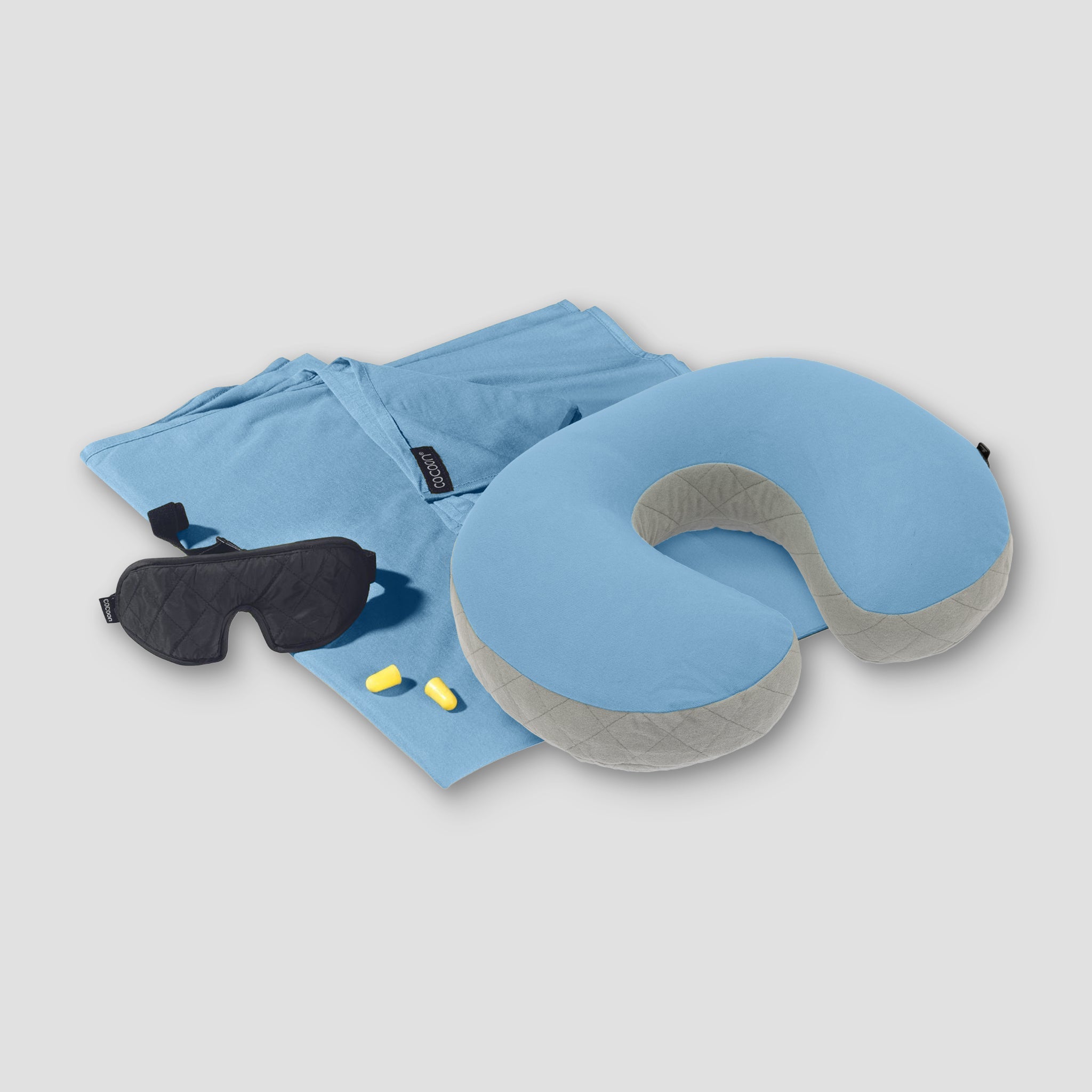 Travel pillow, eye mask, and earplugs on a light gray background